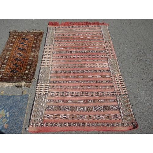 656 - A red ground Rug with striped design 6ft 4in x 3ft 6in, a Saddle Bag and a Wall Hanging