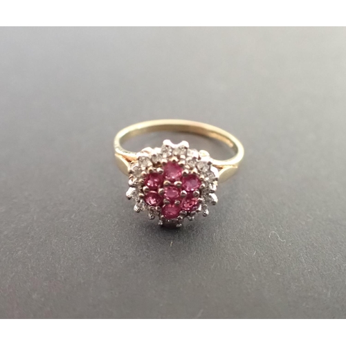 192 - A Ruby Cluster Ring peg-set a group of seven round rubies within a frame of white stones in 9ct gold... 