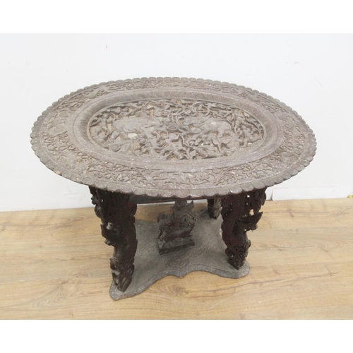 463 - An unusual 19th Century Indian Table, the oval top carved elephants and numerous figures on four dra... 