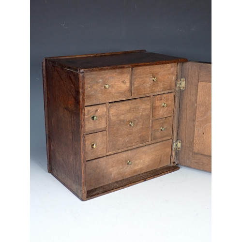 550 - An early 18th Century oak Spice Cupboard with fielded panelled door enclosing eight drawers, 11in sq... 