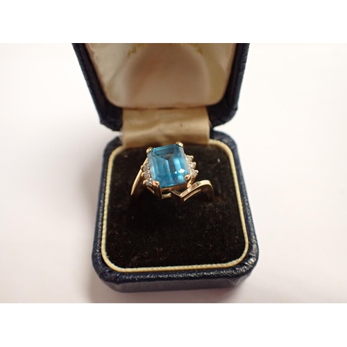 184 - A gold Dress Ring corner claw-set step-cut blue topaz between trios of brilliant-cut diamonds, ring ... 