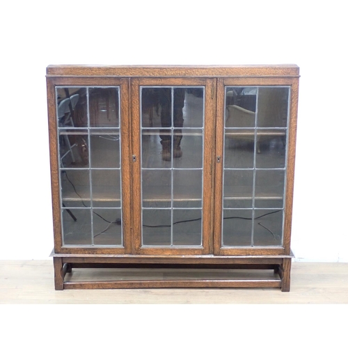 27 - An oak and lead glazed three door Bookcase mounted upon chamfered supports (one pane A/F) 4ft 3in W ... 