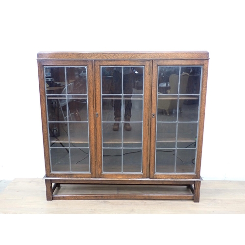 27 - An oak and lead glazed three door Bookcase mounted upon chamfered supports (one pane A/F) 4ft 3in W ... 