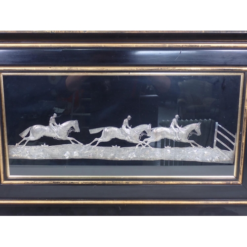 954 - A white metal Panel of three horses racing approaching a fence, 11 x 23in, framed and glazed