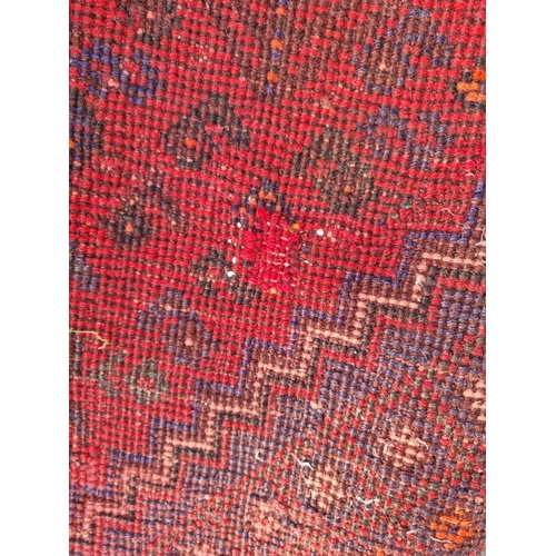 483 - A Persian style woollen red ground Rug with three central dark blue lozenges amongst multiple border... 