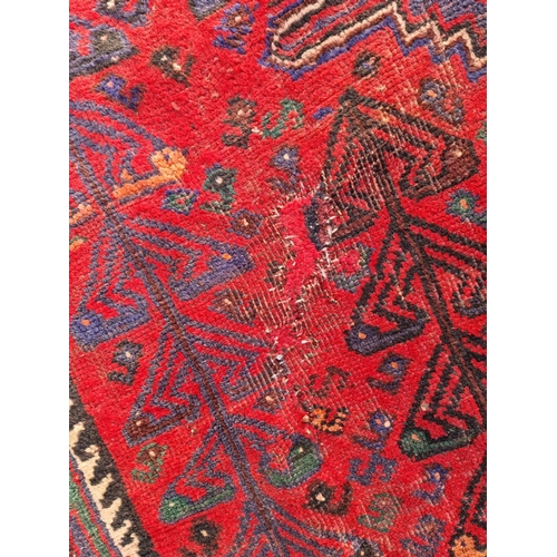 483 - A Persian style woollen red ground Rug with three central dark blue lozenges amongst multiple border... 