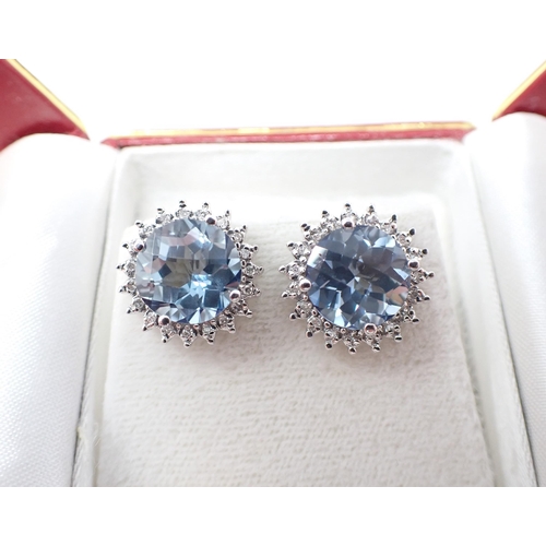 198 - A pair of Blue Topaz and Diamond Cluster Earrings claw-set round multi-faceted topaz within a frame ... 