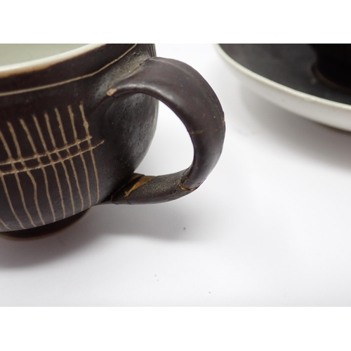 375 - Two Lucie Rie Cups and Saucer in a brown glaze with cream trellis designs, loop handles to the bulbo... 