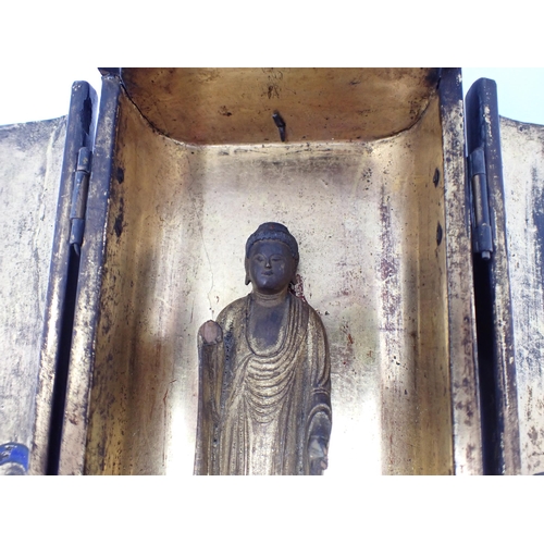 427 - A portable Shrine having laquered finish, two doors open to reveal gilded wooden Buddha on lotus flo... 