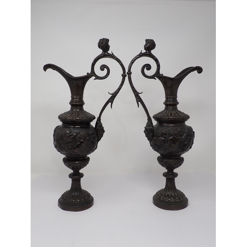 453 - A pair of bronze pedestal Ewers in the classical style, with cherub heads to the scroll handles and ... 