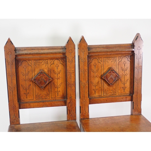 555 - A pair of Arts and Crafts Hall Chairs with arched back supports, carved incised stylised floral desi... 