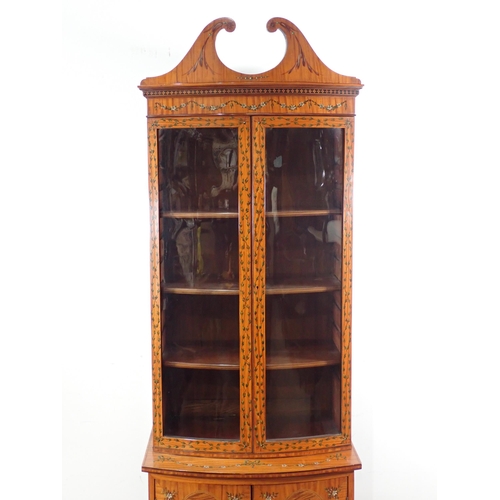 625 - A satinwood bow fronted glazed Cabinet with arched pediment, the upper section fitted adjustable she... 