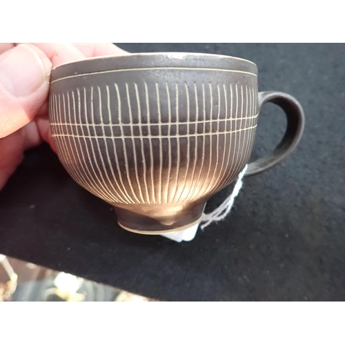 375 - Two Lucie Rie Cups and Saucer in a brown glaze with cream trellis designs, loop handles to the bulbo... 