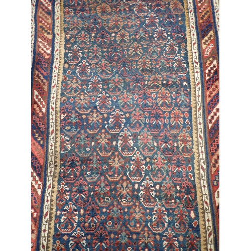 743 - An indigo ground Persian Rug with stylised flowers within striped tramline border 12ft L x 3ft 8in W