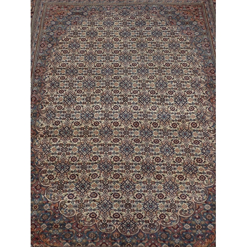 78 - A modern Indo Chahkari Carpet with stylised floral design on cream oval ground within red and blue m... 