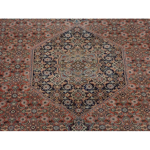 79 - A red ground woollen Carpet with dark blue central hexagon amongst floral decoration 11ft 10in L x 8... 