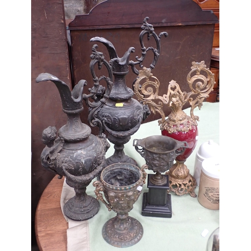 643 - Four cast metal Ewers, a red ceramic two handled Vase with gilt metal handles, a bronze Urn on black... 