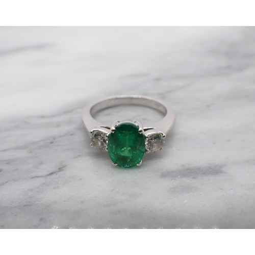 63 - An Emerald and Diamond three stone Ring claw-set oval-cut emerald between two brilliant-cut diamonds... 