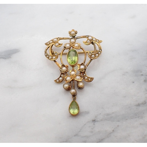 77 - An Edwardian Peridot and Seed Pearl Pendant/Brooch millegrain-set oval-cut peridot within scrolled o... 