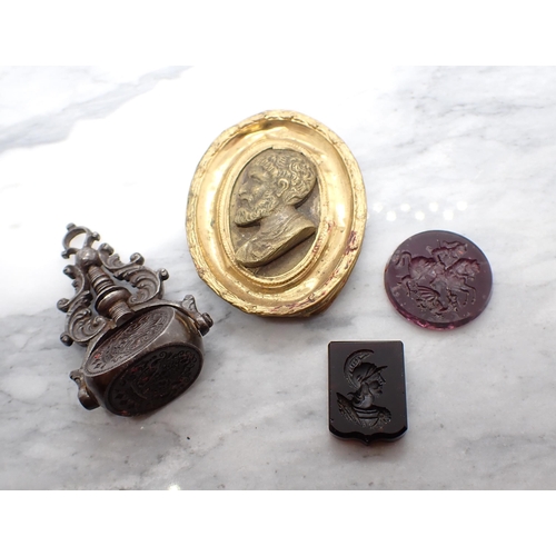 127 - Two amethyst coloured Intaglio Seals, a swivel Fob bearing three crest seals and a Miniature of clas... 