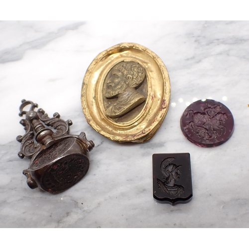 127 - Two amethyst coloured Intaglio Seals, a swivel Fob bearing three crest seals and a Miniature of clas... 