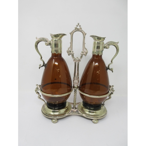 211 - A pair of amber glass Claret Jugs with plated mounts, scroll handles on a plated stand with central ... 