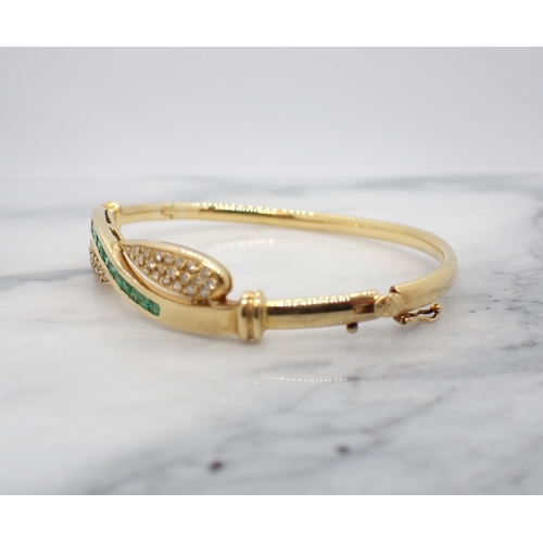 28 - An Emerald and Diamond hinged Bangle the front with crossover design channel-set a row of calibré-cu... 