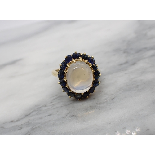 163 - A Moonstone and sapphire Cluster Ring claw-set oval moonstone cabochon within a frame of cushion-cut... 