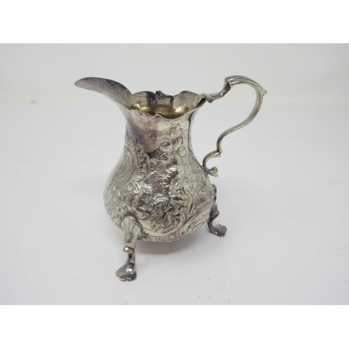 99 - A Georgian silver Cream Jug with floral embossing on three pad feet, marks worn