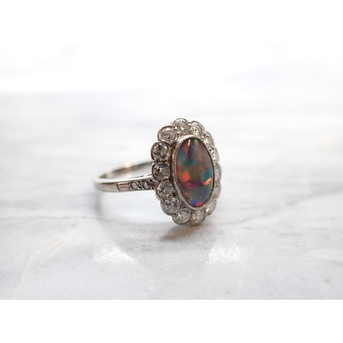 250 - A Black Opal and Diamond Cluster Ring millegrain-set oval opal within a frame of brilliant-cut diamo... 