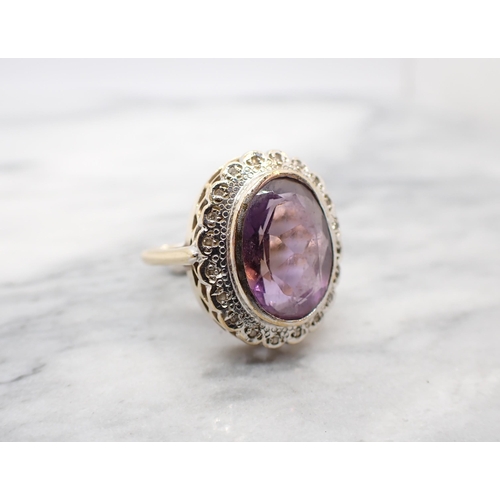 285 - An Amethyst and Diamond Cluster Ring rubover-set oval-cut amethyst within a frame of illusion-set ei... 