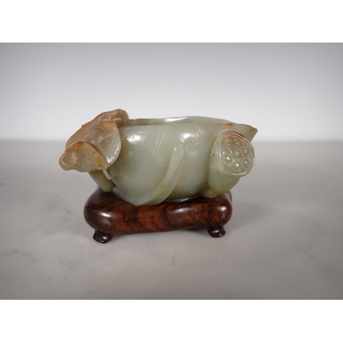 404 - An Oriental jade lotus blossom Bowl with carved leafage design on a hardwood stand, 4 in long