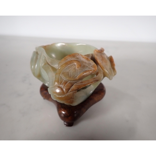 404 - An Oriental jade lotus blossom Bowl with carved leafage design on a hardwood stand, 4 in long