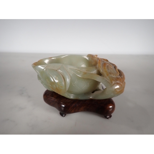 404 - An Oriental jade lotus blossom Bowl with carved leafage design on a hardwood stand, 4 in long