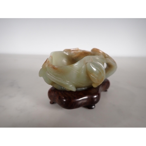 404 - An Oriental jade lotus blossom Bowl with carved leafage design on a hardwood stand, 4 in long