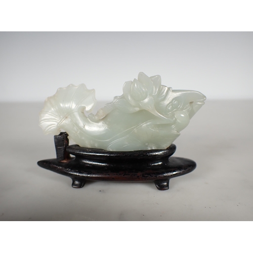 413 - A Chinese celadon Jade carved Fish with lily pad and flower to one side, small chips, on hardwood st... 