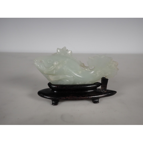 413 - A Chinese celadon Jade carved Fish with lily pad and flower to one side, small chips, on hardwood st... 