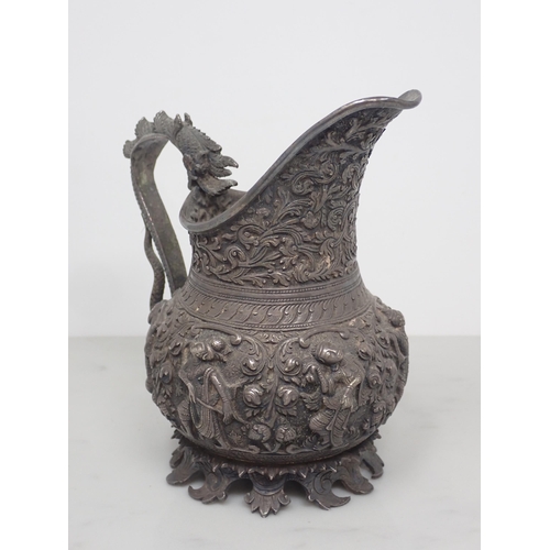 66 - An antique Burmese silver jug, decorated with a band of high relief repousse mythological figures, w... 