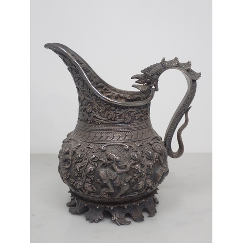 66 - An antique Burmese silver jug, decorated with a band of high relief repousse mythological figures, w... 