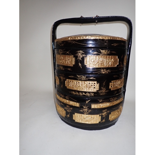 677 - An Oriental black lacquered and gilt three tier cylindrical storage box decorated birds and flowerin... 