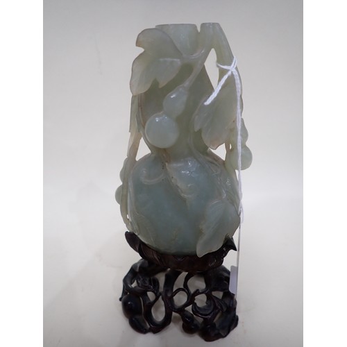 405 - An Oriental carved jade lidded Bottle vase with leafage and fruit decoration, on a carved hardwood s... 