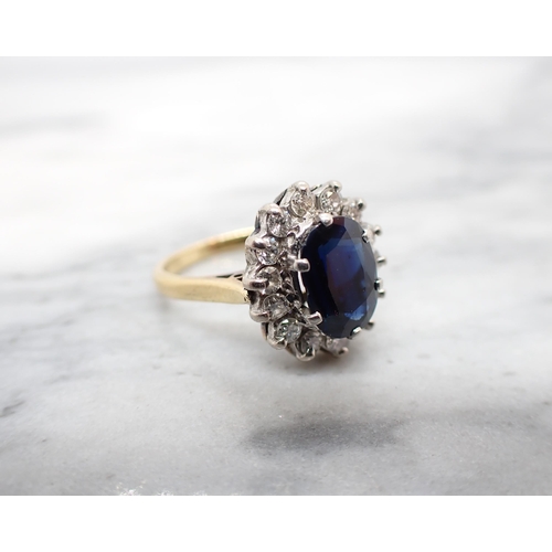 181 - A Sapphire and Diamond Cluster Ring claw-set oval-cut sapphire within a frame of fourteen brilliant-... 