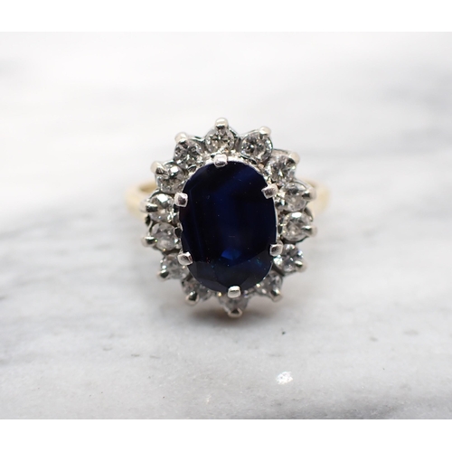 181 - A Sapphire and Diamond Cluster Ring claw-set oval-cut sapphire within a frame of fourteen brilliant-... 