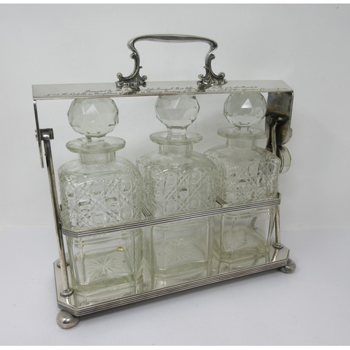 106 - A silver plated Tantalus fitted three square cut glass Decanters and Stoppers, reeded rim on ball fe... 