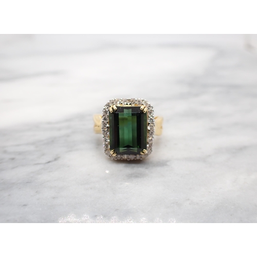 167 - A Green Tourmaline and Diamond Cluster Ring corner claw-set step-cut tourmaline within a frame of br... 