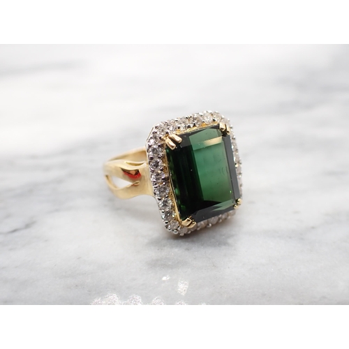 167 - A Green Tourmaline and Diamond Cluster Ring corner claw-set step-cut tourmaline within a frame of br... 