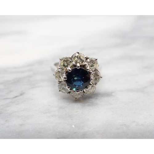 198 - A Sapphire and Diamond Flower Cluster Ring claw-set round sapphire within a frame of eight brilliant... 