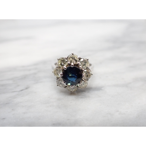 198 - A Sapphire and Diamond Flower Cluster Ring claw-set round sapphire within a frame of eight brilliant... 