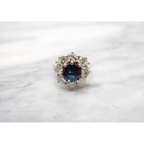 198 - A Sapphire and Diamond Flower Cluster Ring claw-set round sapphire within a frame of eight brilliant... 