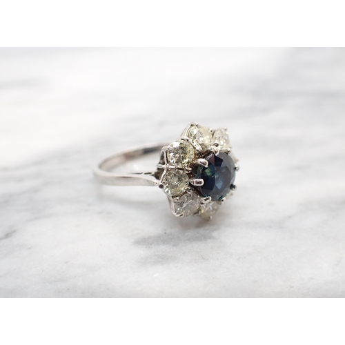 198 - A Sapphire and Diamond Flower Cluster Ring claw-set round sapphire within a frame of eight brilliant... 